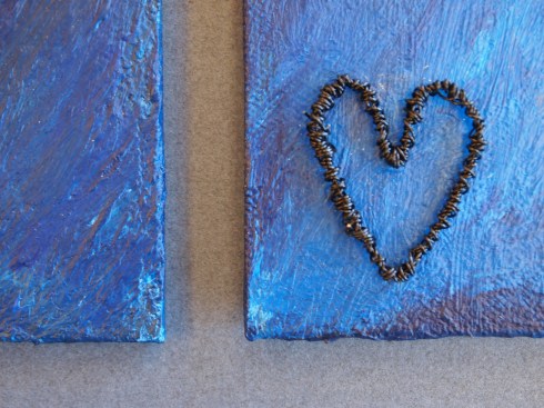 Maalauksen symbolit on tehty rautalangasta ja ne nousevat koholleen kuvapinnasta.